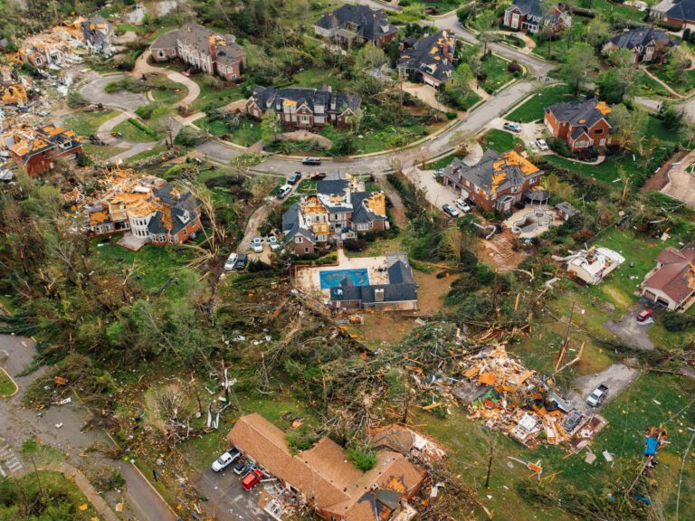 Vue aérienne d'un quartier résidentiel dévasté par une tornade, toitures arrachées et arbres couchés