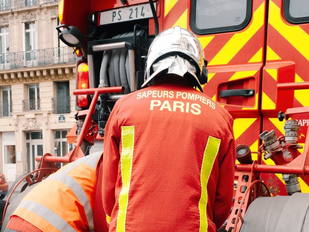 Sapeur-pompier de Paris de dos, en tenue d'intervention, devant un fourgon incendie dans une rue parisienne