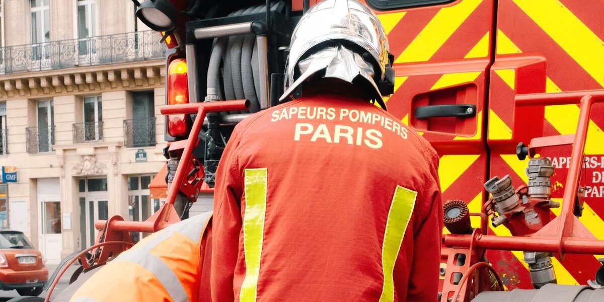 Sapeur-pompier de Paris de dos, en tenue d'intervention, devant un fourgon incendie dans une rue parisienne